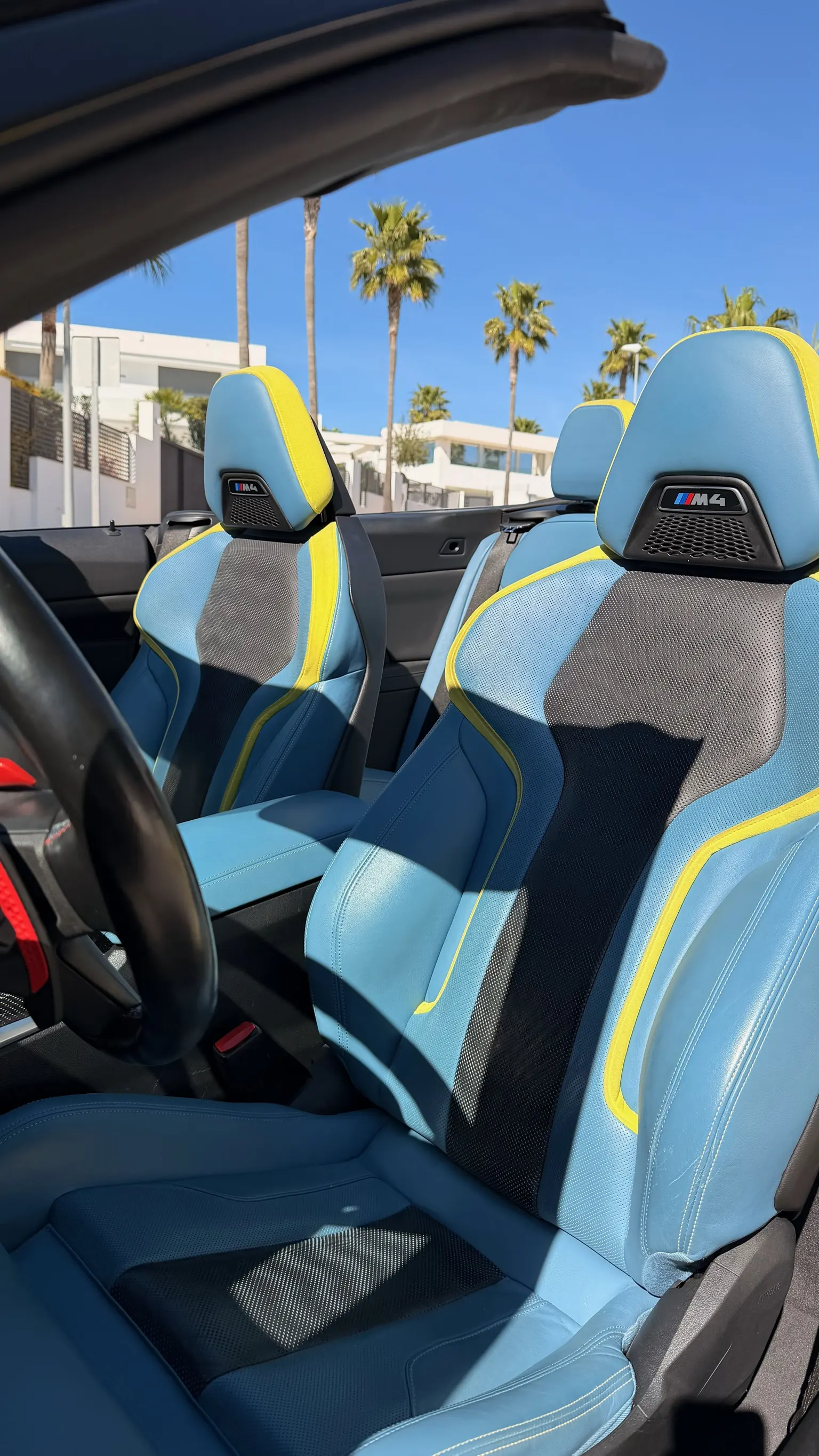 Close-up of M4 bucket seats in light blue leather and perforated Alcantara with yellow accents and illuminated M4 badge, BMW Individual interior