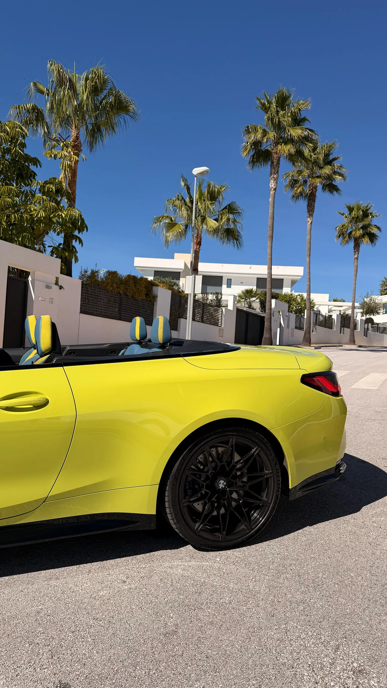 Rear three-quarter view of the yellow BMW M4 Convertible with black M wheel and visible blue and yellow BMW Individual leather interior