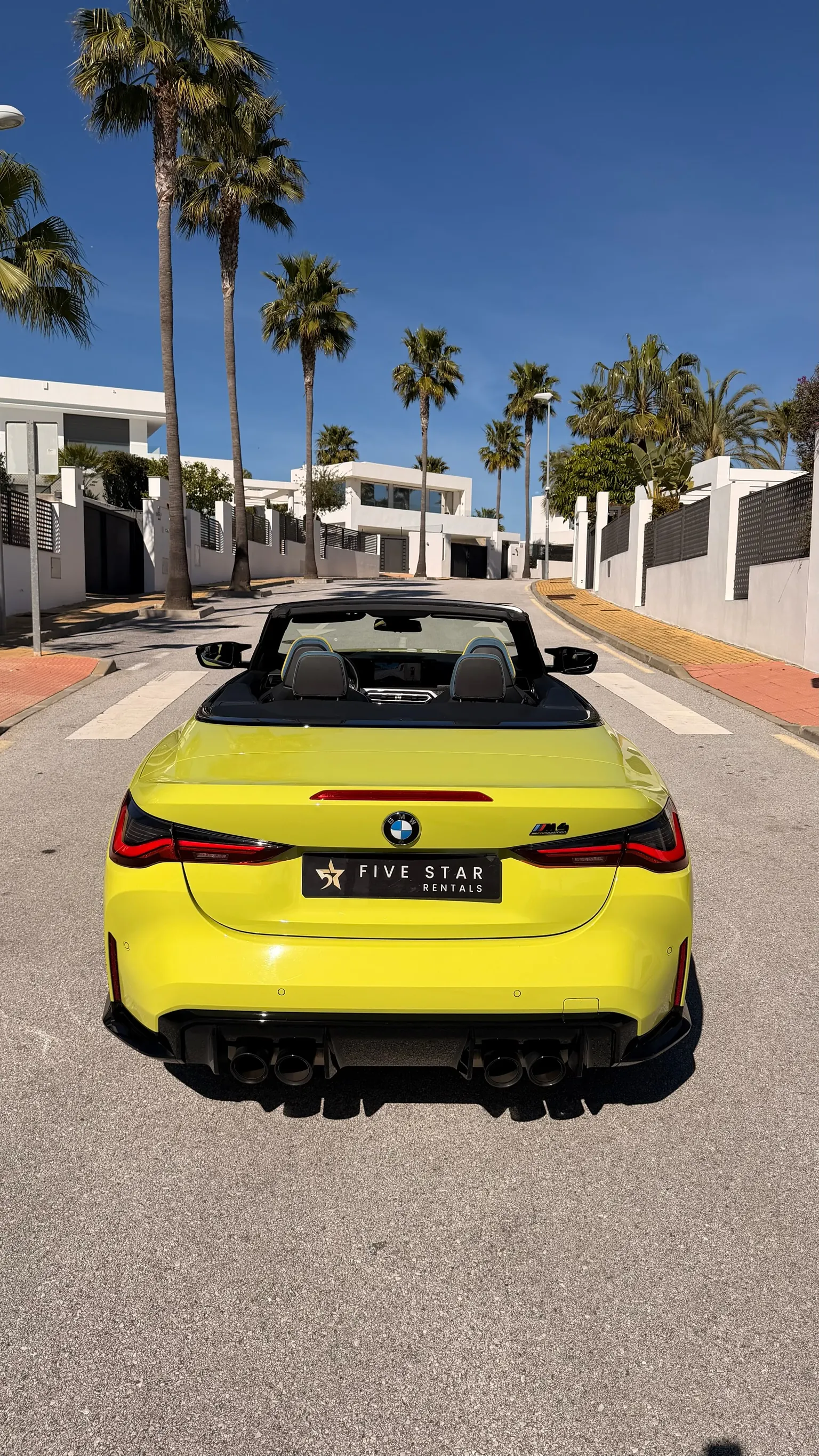 Centered rear view of the yellow BMW M4 Competition Convertible with quad exhaust, M4 Competition badge and Five Star Rentals plate