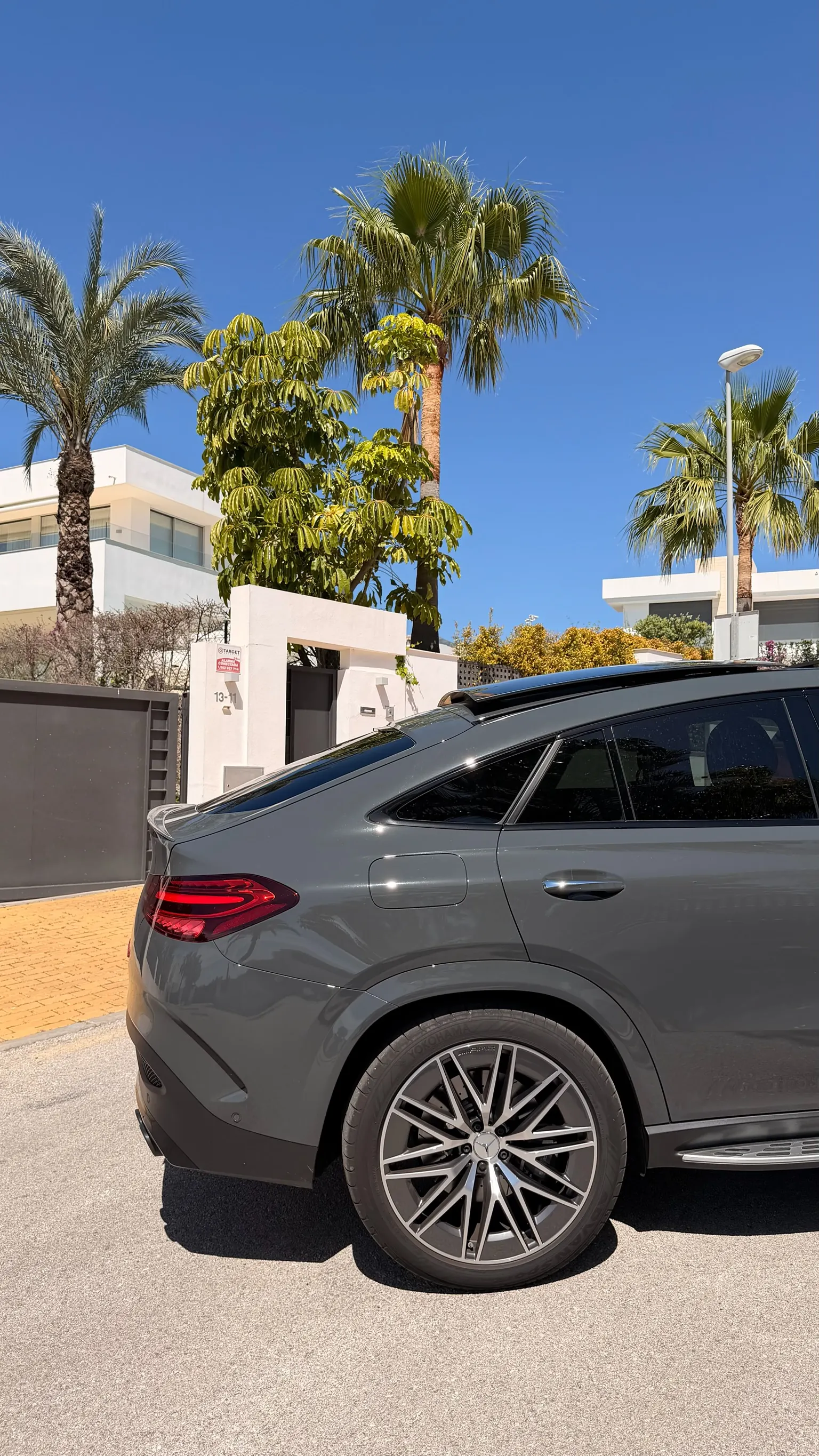 Rear side profile of the Selenite Grey Mercedes-AMG GLE 53 Coupé with integrated roof spoiler and 22-inch two-tone AMG wheel