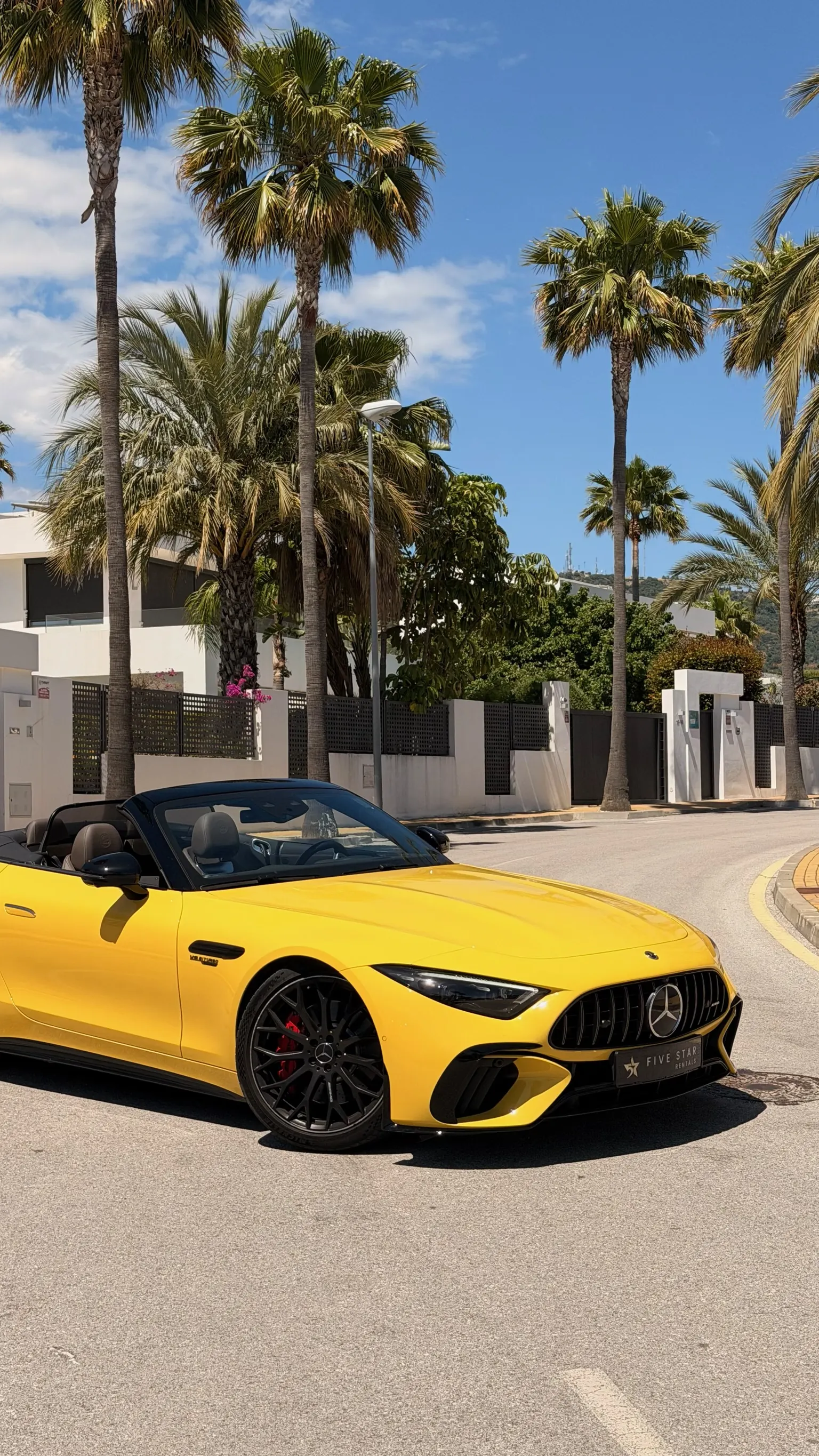 Close-up front three-quarter view of the Sun Yellow Mercedes-AMG SL 55 with Five Star Rentals plate, V8 BITURBO fender badge, matte black cross-spoke wheels and red Brembo calipers