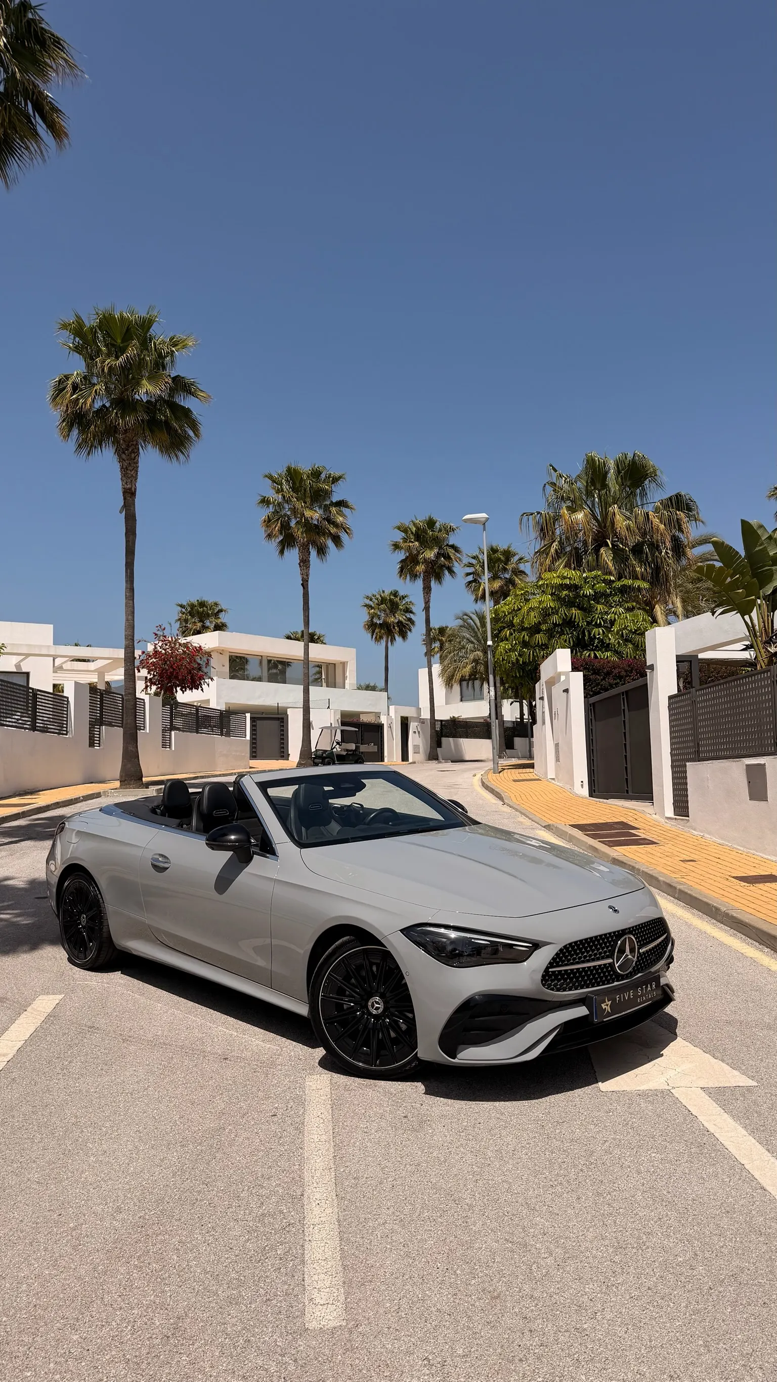 Mercedes-Benz CLE 200 Cabriolet AMG Line in Alpine Grey, top-down front three-quarter view with Five Star Rentals plate and Marbella palm trees