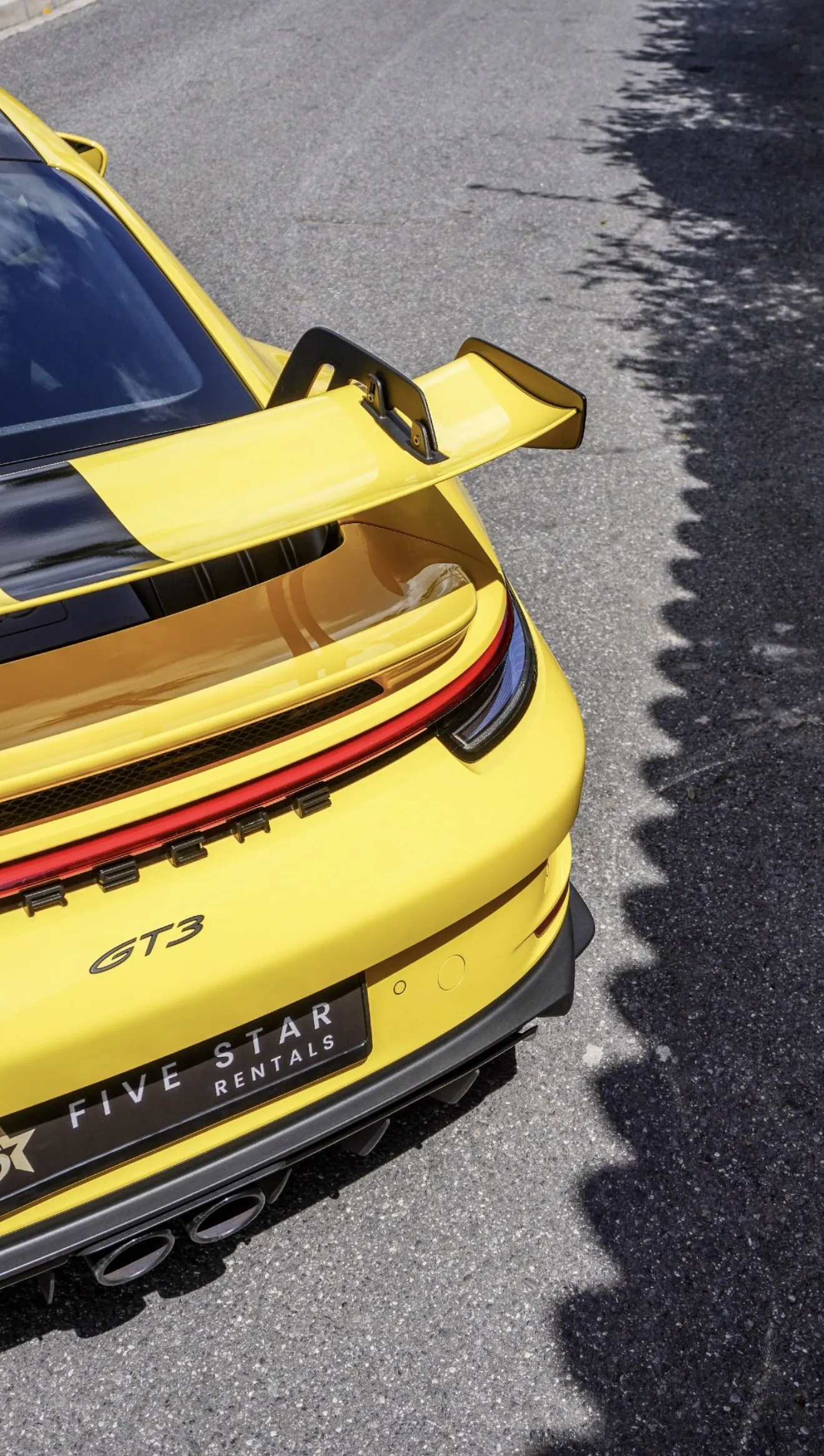 Top-down rear detail of the Racing Yellow Porsche 911 GT3 992 with swan-neck wing, red LED light bar, GT3 badge and central dual exhaust