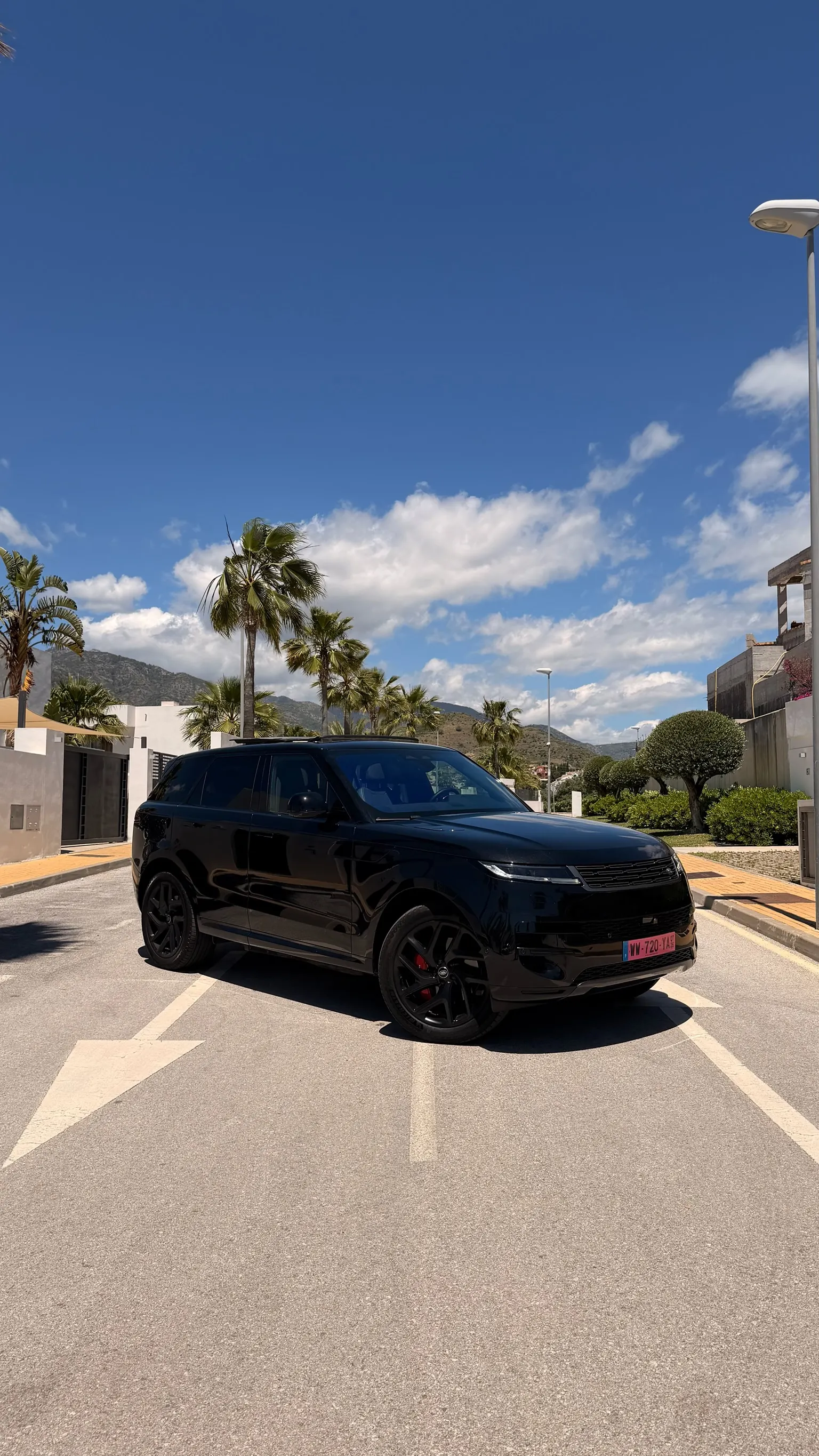 Range Rover Sport P460e in Santorini Black, front three-quarter view with 22-inch black wheels, red brake calipers and Marbella palm trees